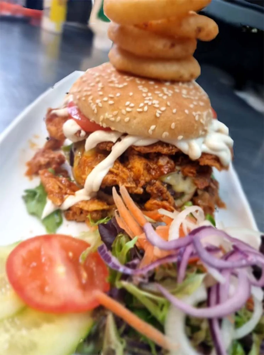 A battered chicken burger in a seeded bun with salad and sauce.