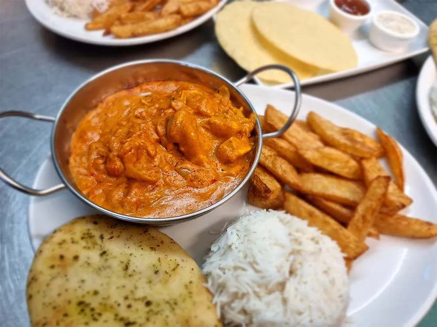 A curry in a balti dish with naan bread, rice and chips.