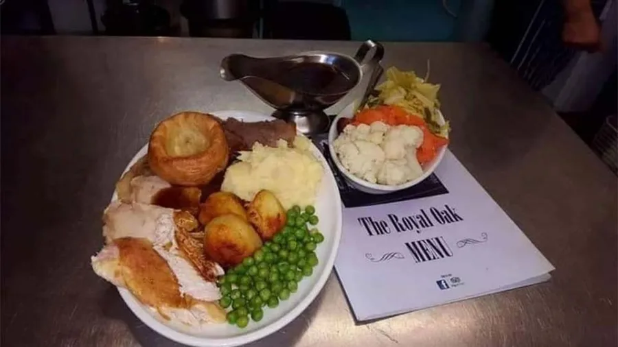 A Sunday roast with Yorkshire pudding, roast potatoes and peas beside a Royal Oak menu card.